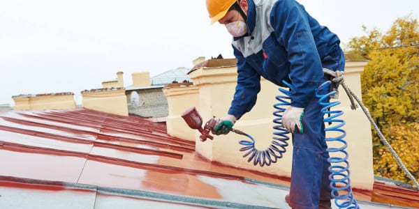 man painting roof with paint gun